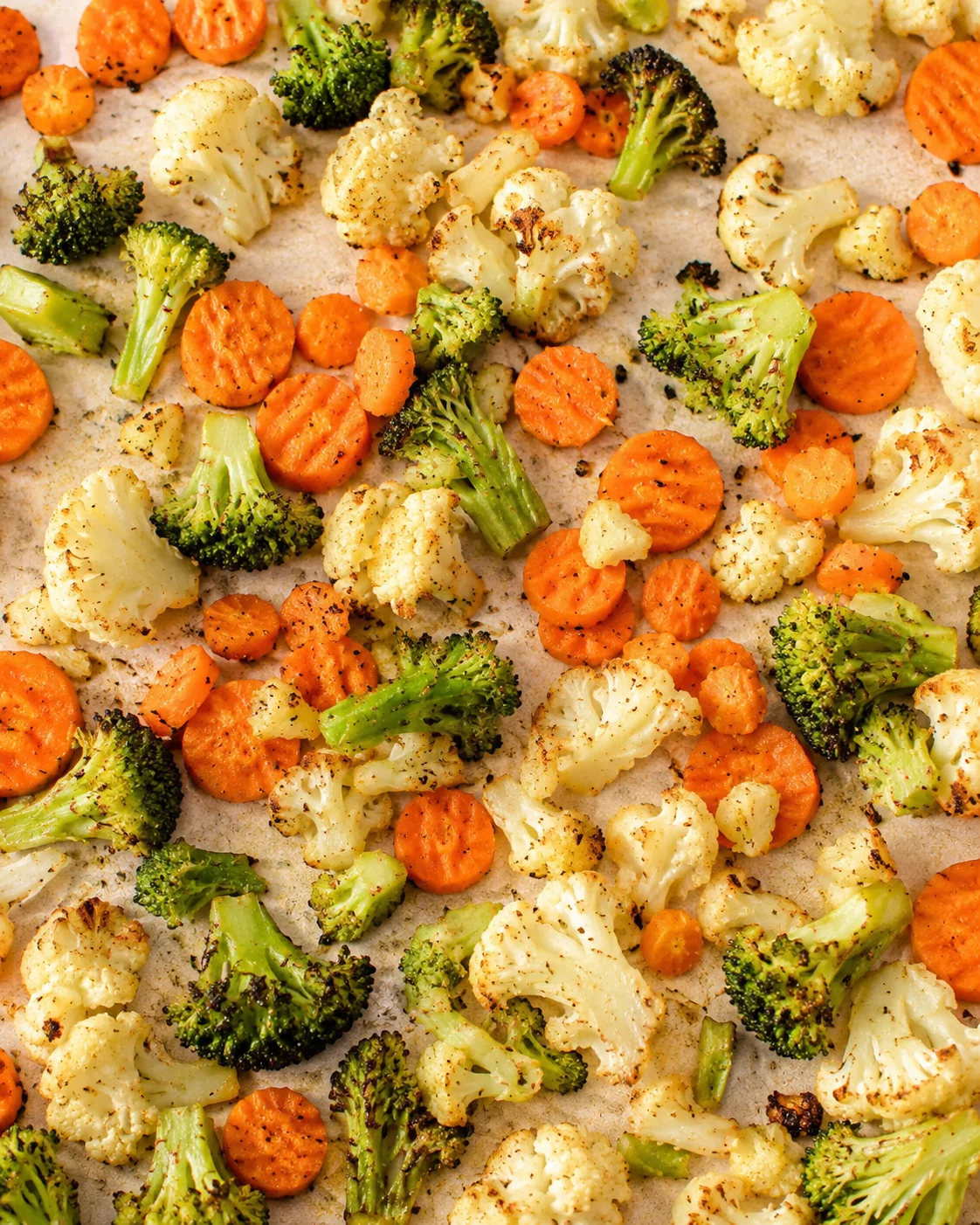 roasted broccoli, cauliflower, and carrot florets spread on a parchment-lined baking sheet