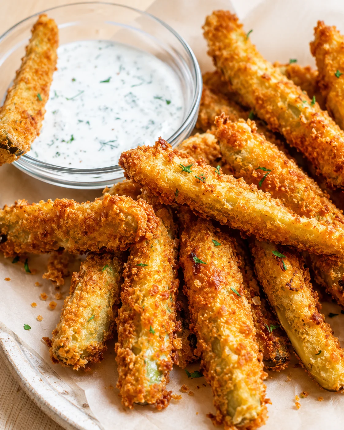 Golden-brown zucchini fries with a ranch dip in a glass bowl on parchment