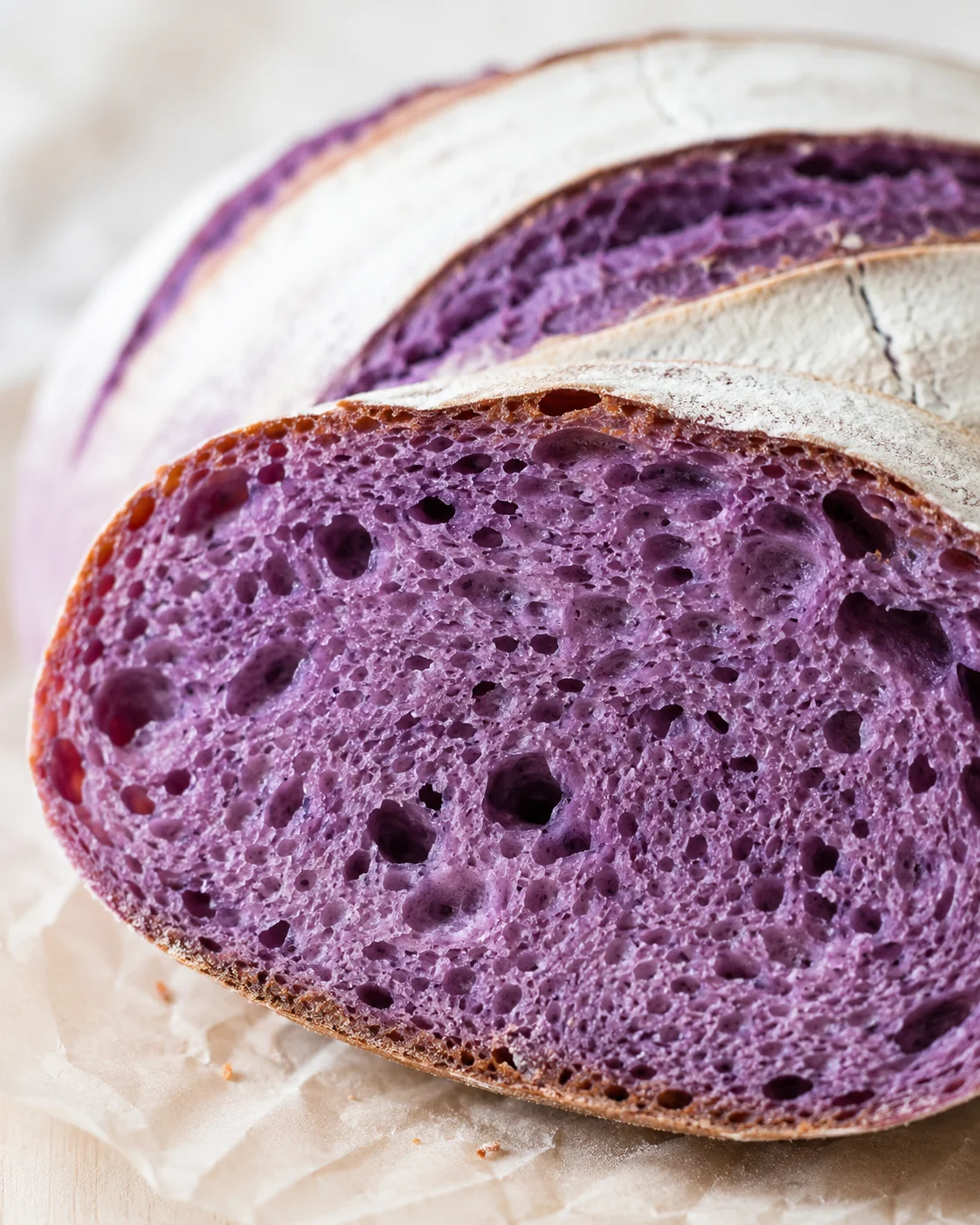 close-up of purple-ube bread slices with airy crumb and flour-dusted crust on parchment