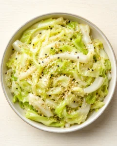 bowl of glossy napa cabbage with sesame seeds on a light wooden surface