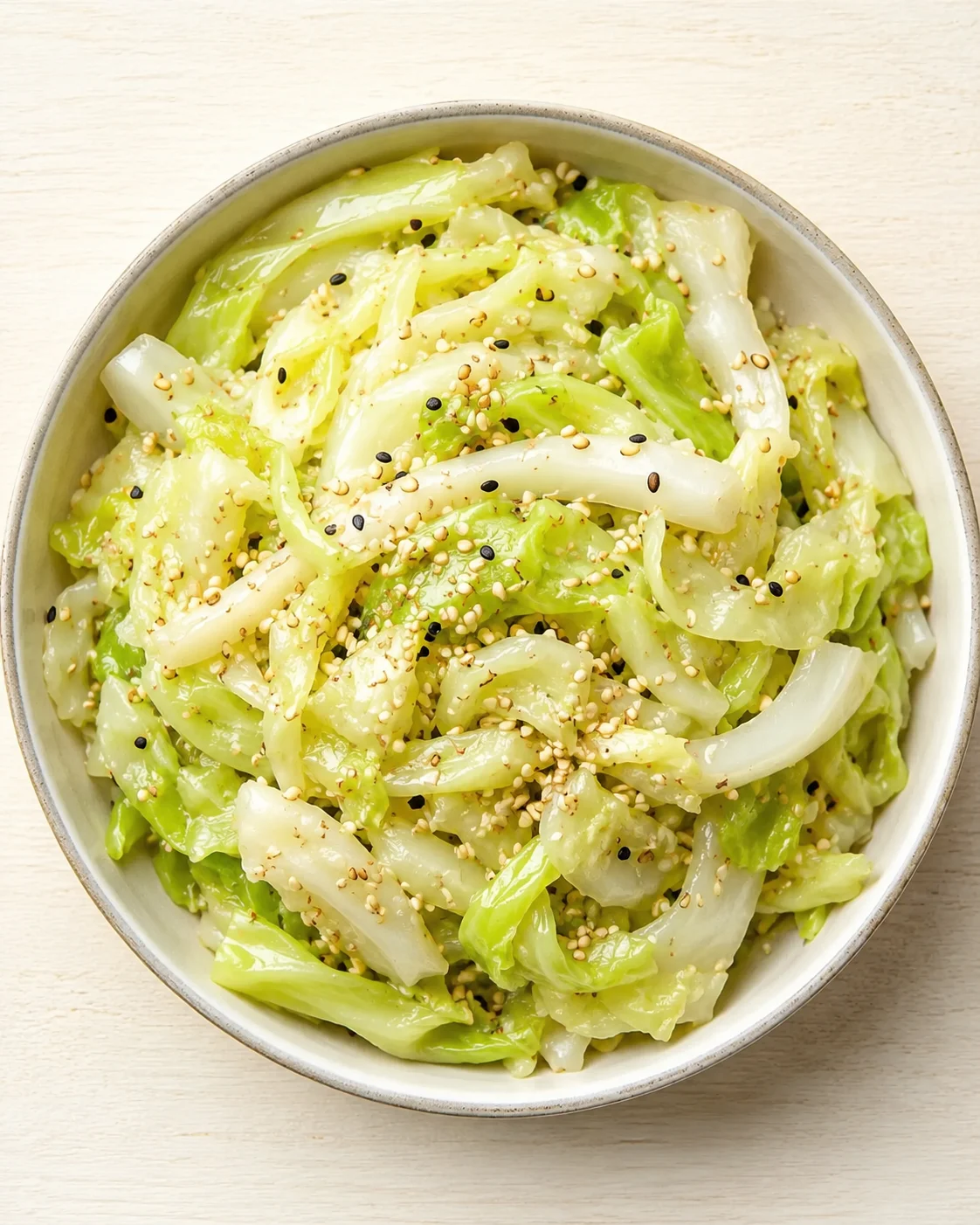 bowl of glossy napa cabbage with sesame seeds on a light wooden surface