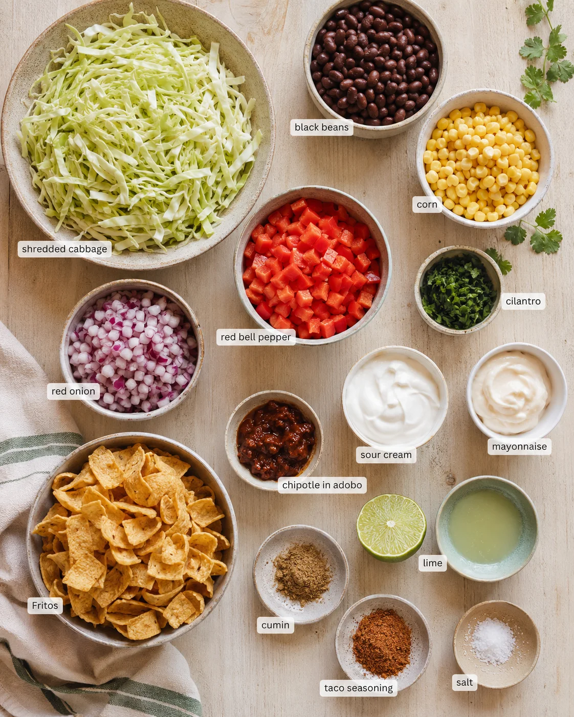 Overhead view of bowls with shredded cabbage, beans, corn, peppers, onions, cilantro, and sauces.