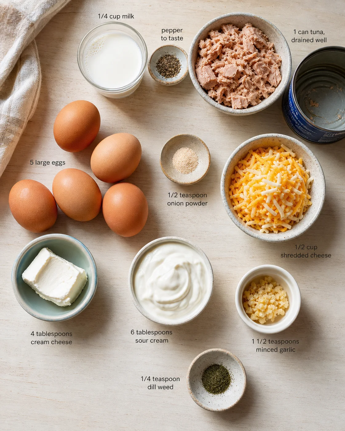Overhead view of labeled tuna recipe ingredients laid out on a light wooden surface.