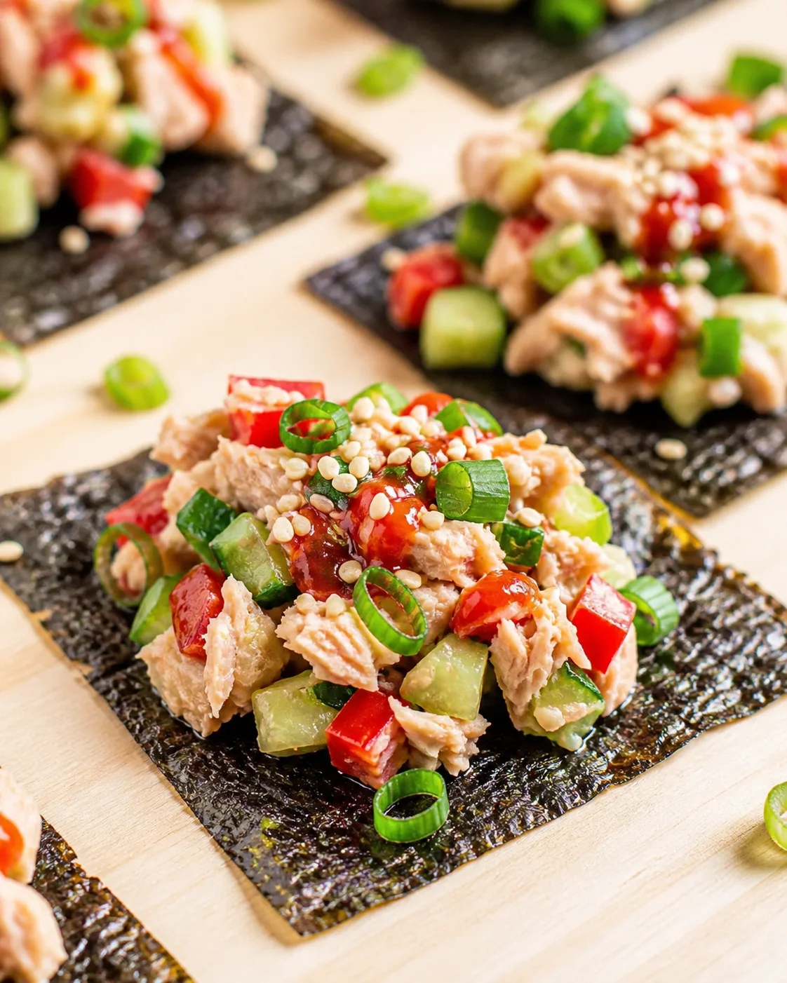 Tuna salad atop nori squares with cucumber and red pepper, sesame seeds, and green onion rings