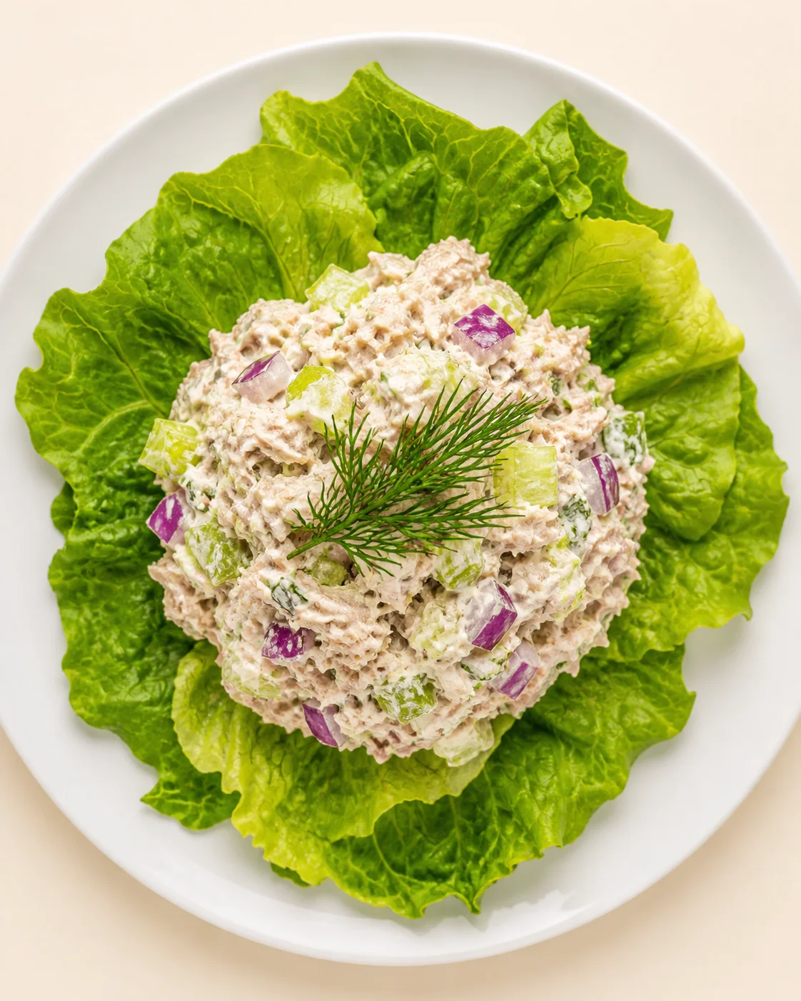 Overhead view of creamy tuna salad on bright lettuce leaves, garnished with dill and diced red onion.