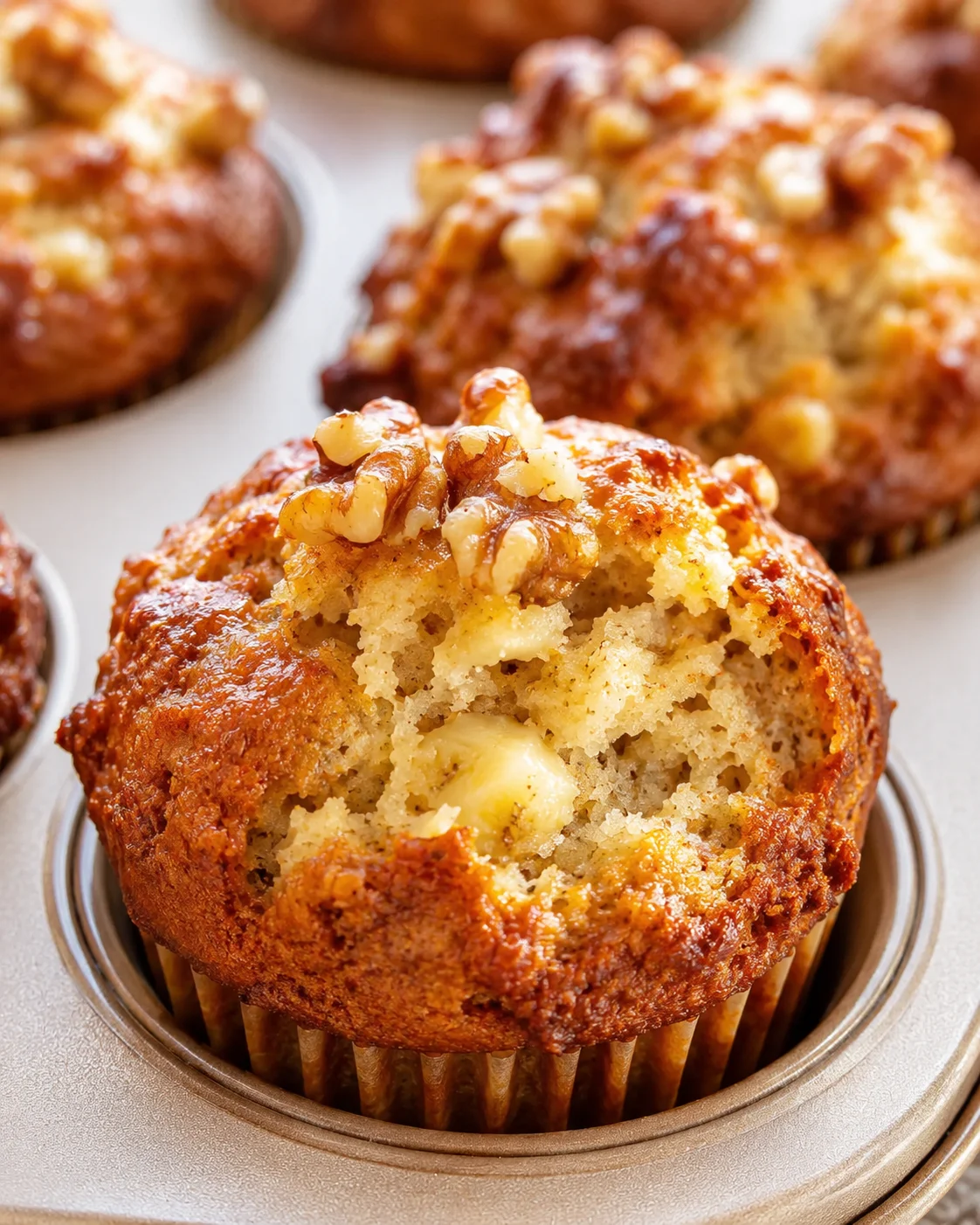 Close-up of walnut-topped cheddar muffins in a metal muffin tin, showing crumbly interior and glossy nut topping.