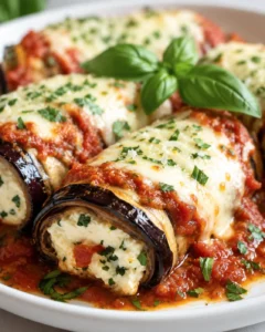 Close-up of cheesy, rolled eggplant slices topped with herbs on a white plate