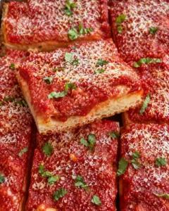 Close-up of baked Sicilian tomato pie topped with cheese and fresh herbs.