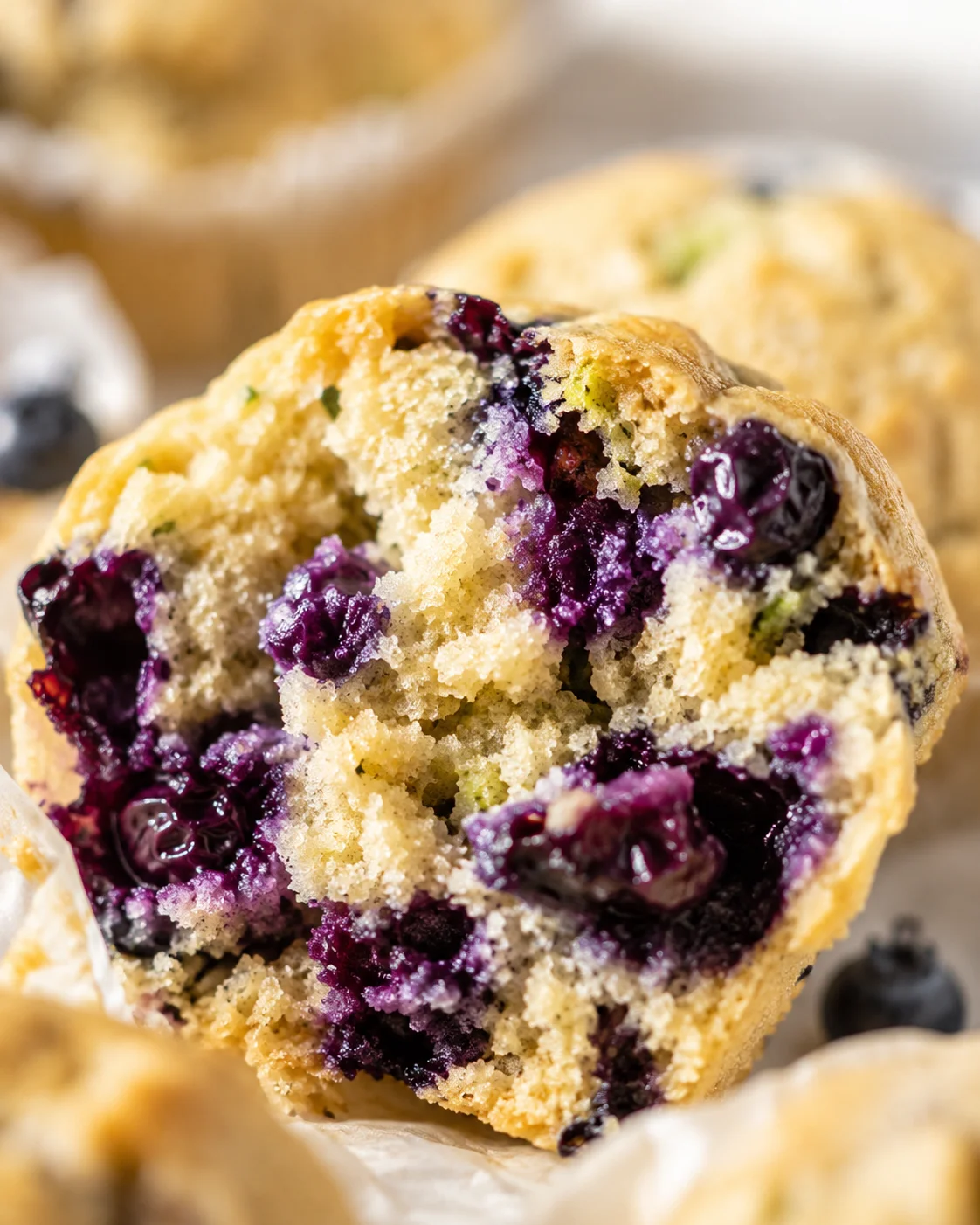 Close-up of a broken blueberry muffin showing purple blueberry pockets inside a golden crumb