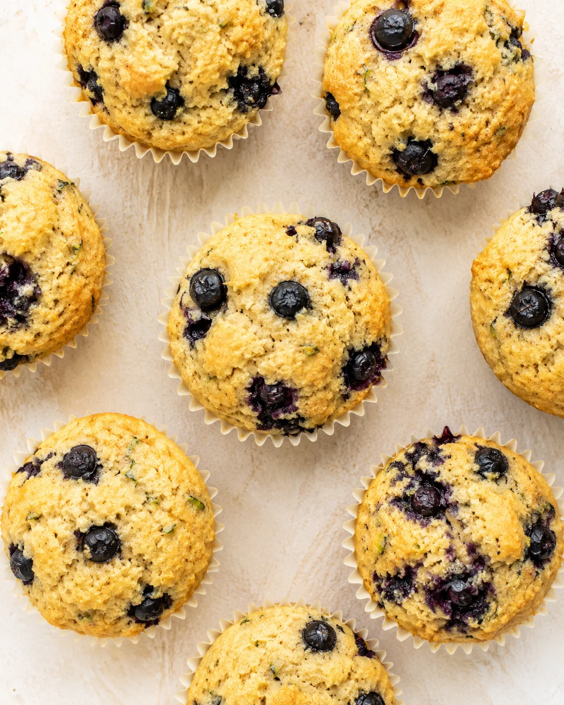 Top-down view of blueberry muffins in paper liners on a light wooden surface.