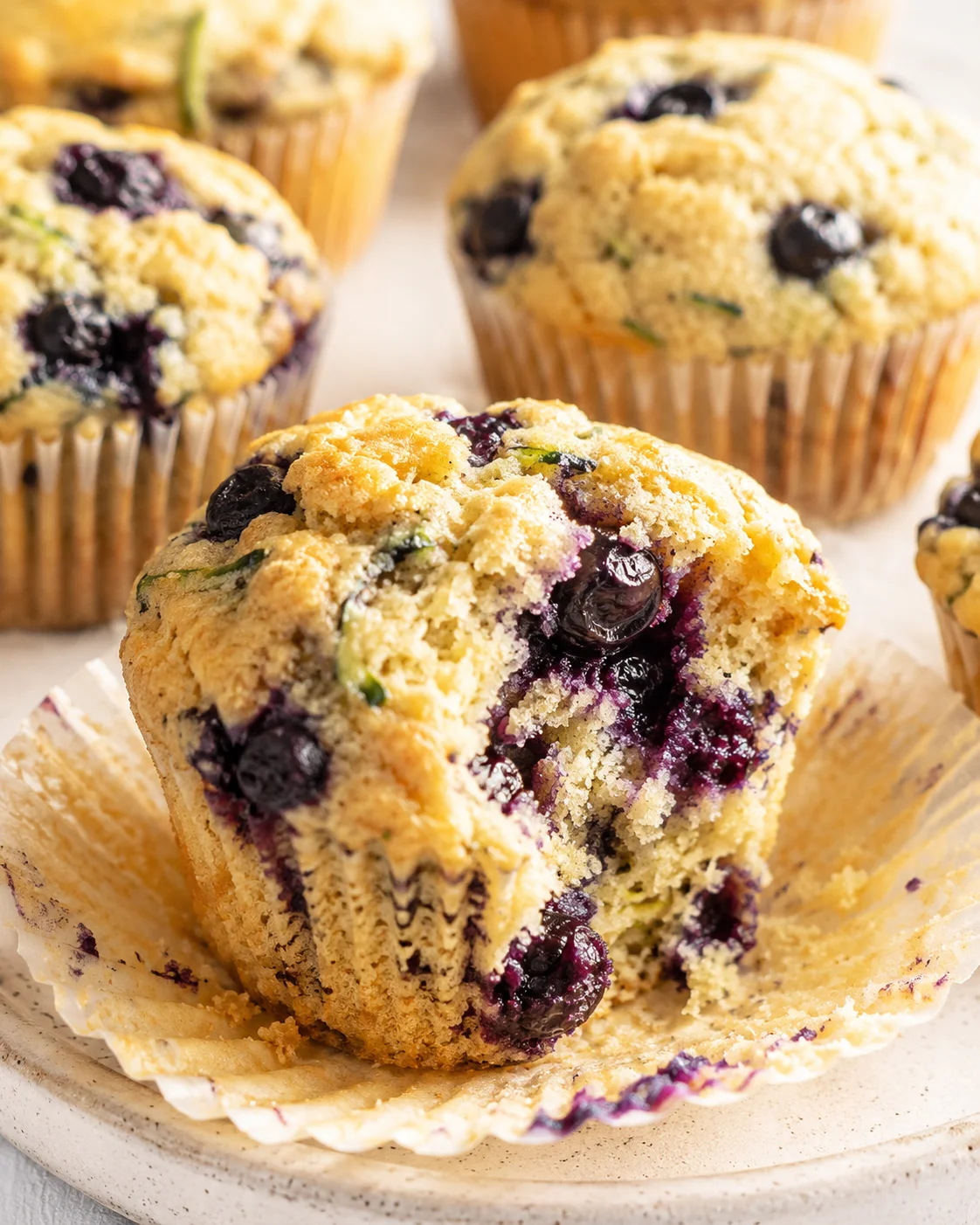 Close-up of blueberry muffins with crumb topping, bitten muffin in foreground on a plate.