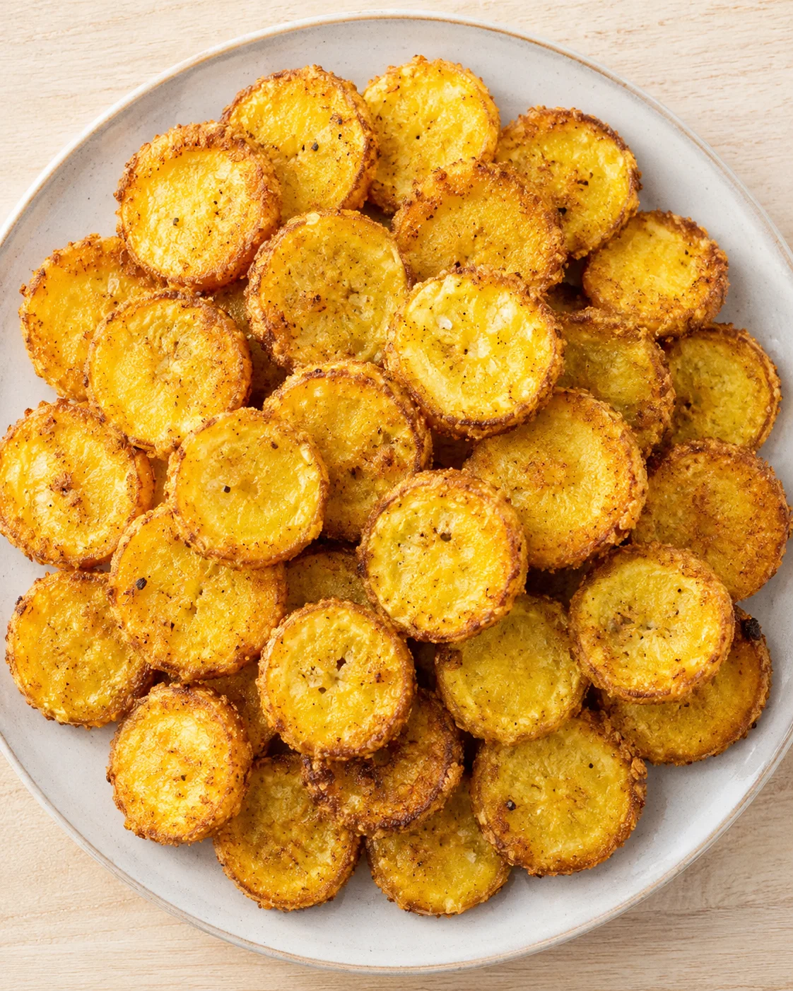 Small, round, golden-brown fried potato coins piled on a light plate