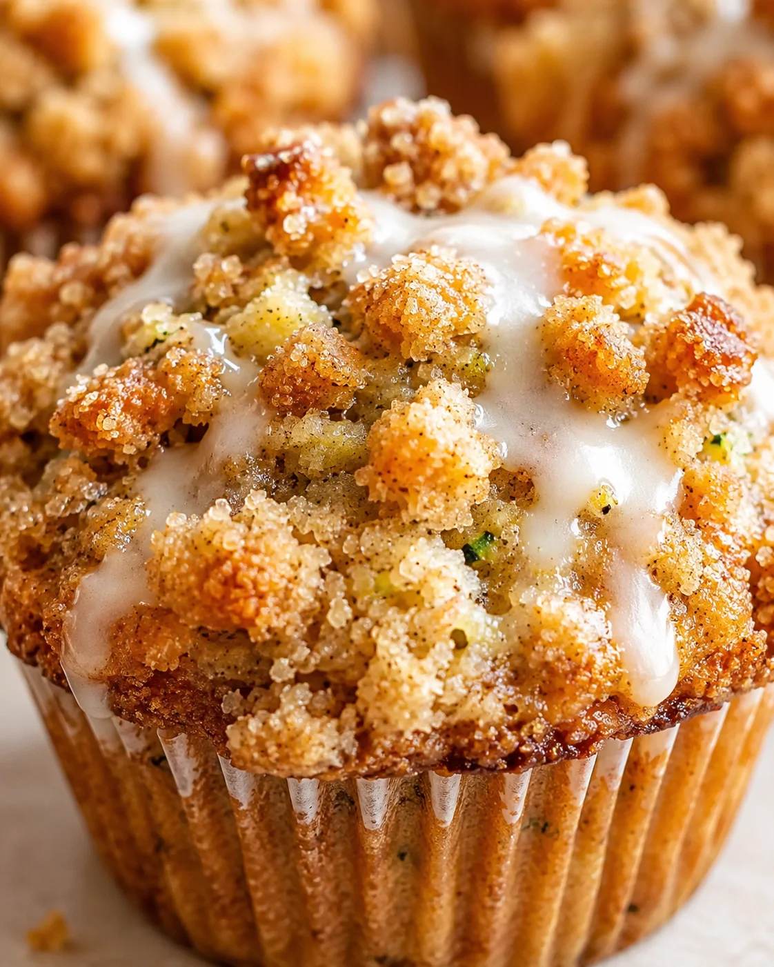 Close-up of a crumb-topped muffin with glossy white glaze drizzled over the top.