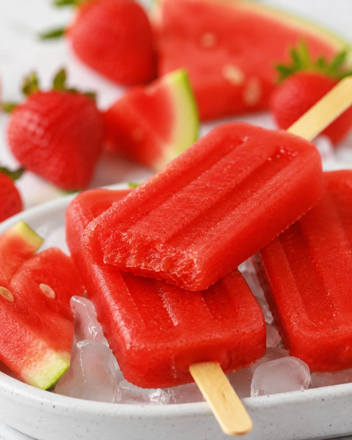 Close-up of vibrant homemade strawberry watermelon popsicles on ice with fresh fruit around