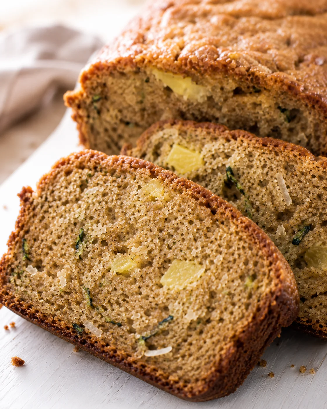 Close-up of moist pineapple coconut zucchini bread with slices on a white surface