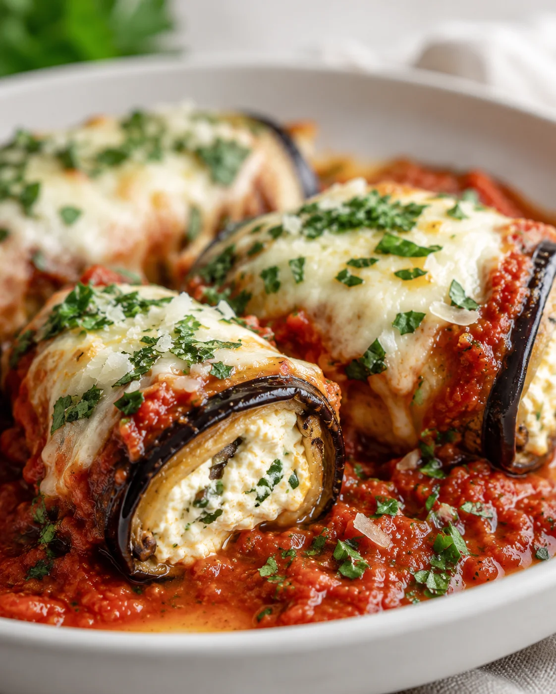Delicious baked eggplant rollatini topped with cheese and fresh herbs on a white plate