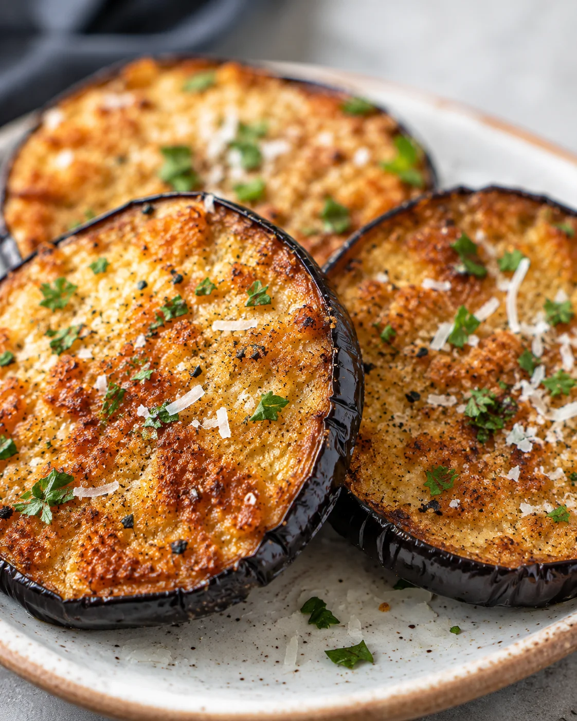 Golden, crispy eggplant slices topped with herbs and cheese, served on a white plate