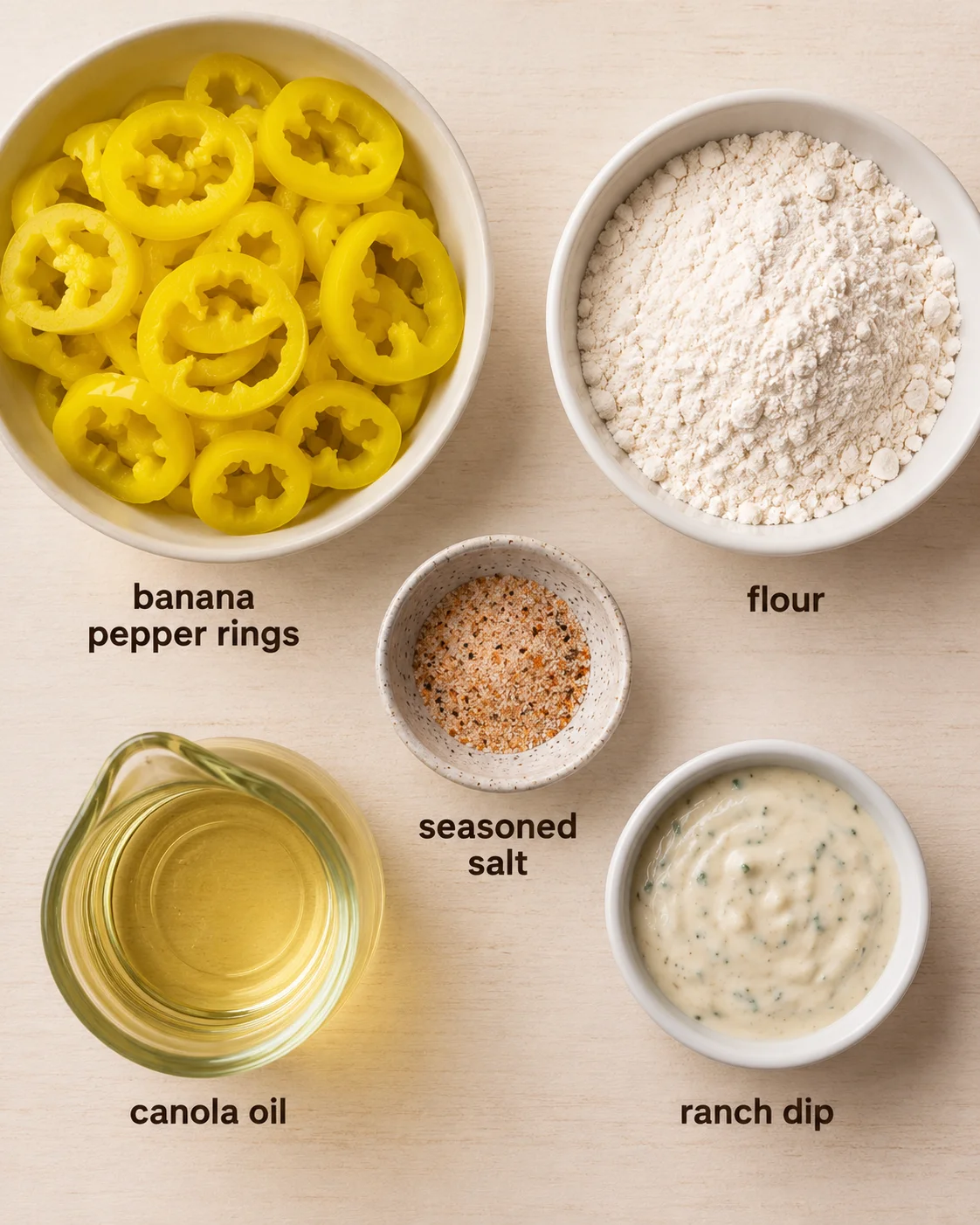 Bowl of yellow banana pepper rings with flour, seasoning, oil, and ranch dip nearby