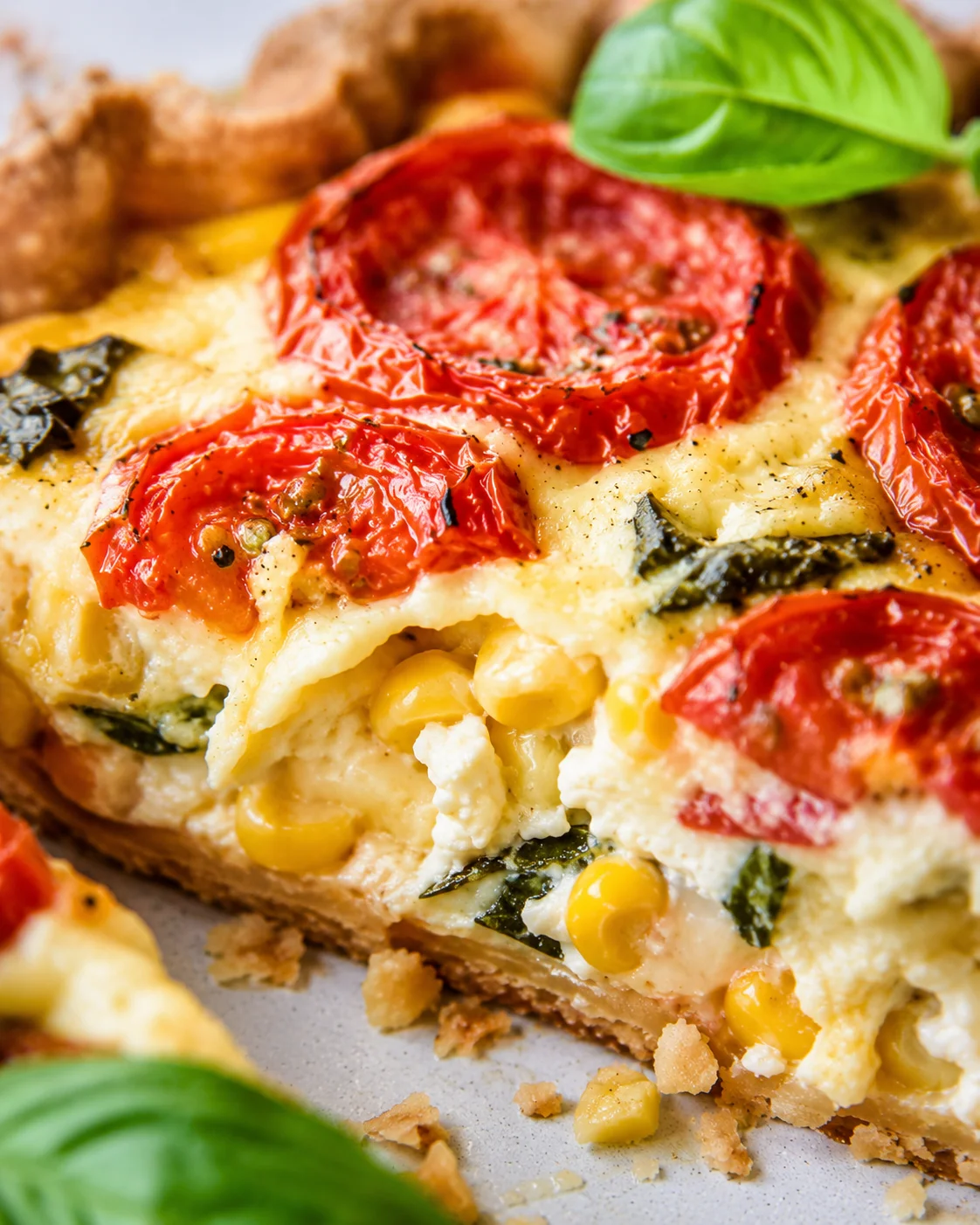 Close-up of a savory tomato pie topped with roasted tomatoes, basil, and cheese.