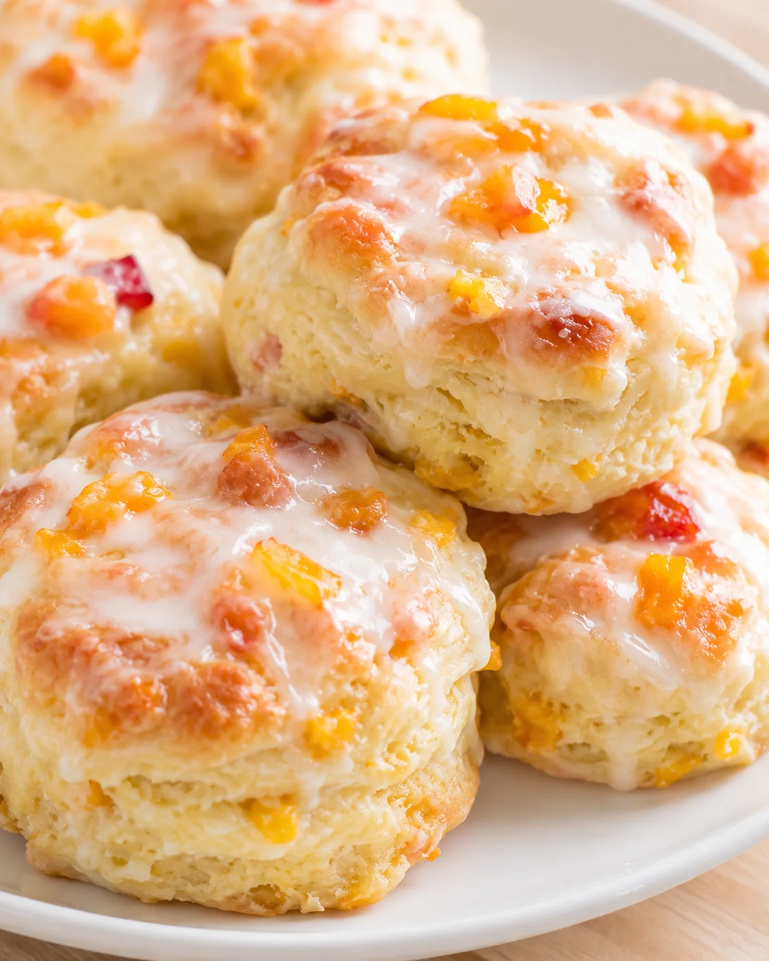 Fluffy peach-filled biscuits topped with white glaze on a white plate