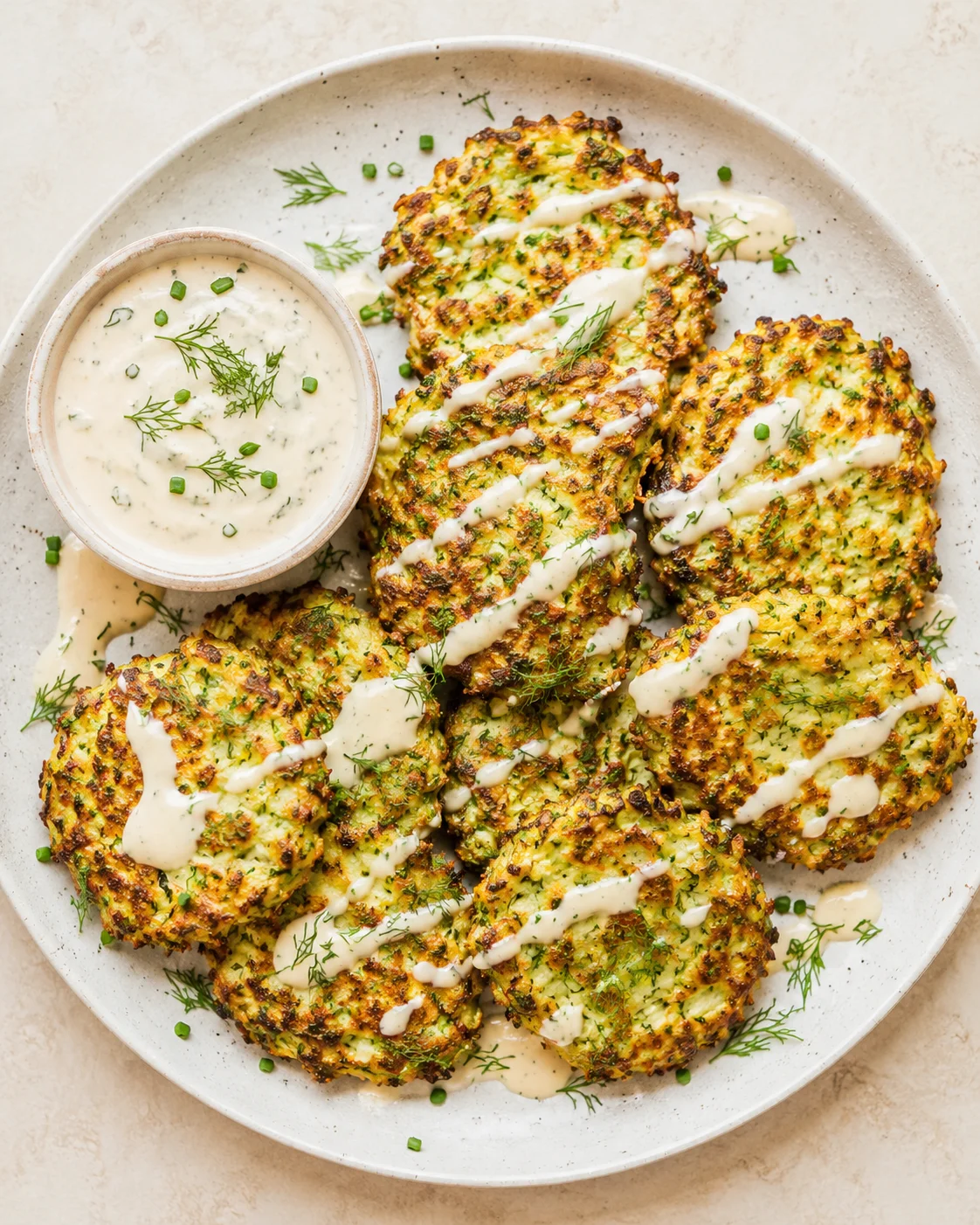 Crispy zucchini fritters on a plate, drizzled with dill-scented creamy sauce and herbs.