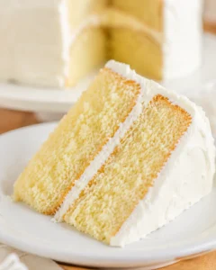 Slice of homemade vanilla cake with creamy frosting on a white plate