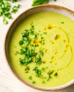 A bowl of vibrant green creamy zucchini soup garnished with fresh herbs and olive oil.