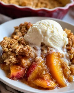 Freshly baked nectarine crisp topped with vanilla ice cream on a white plate.