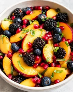 Vibrant fruit salad with peaches, blackberries, blueberries, pomegranate seeds, and basil