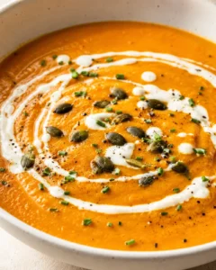 Creamy roasted carrot and ginger soup garnished with seeds and herbs in a bowl.