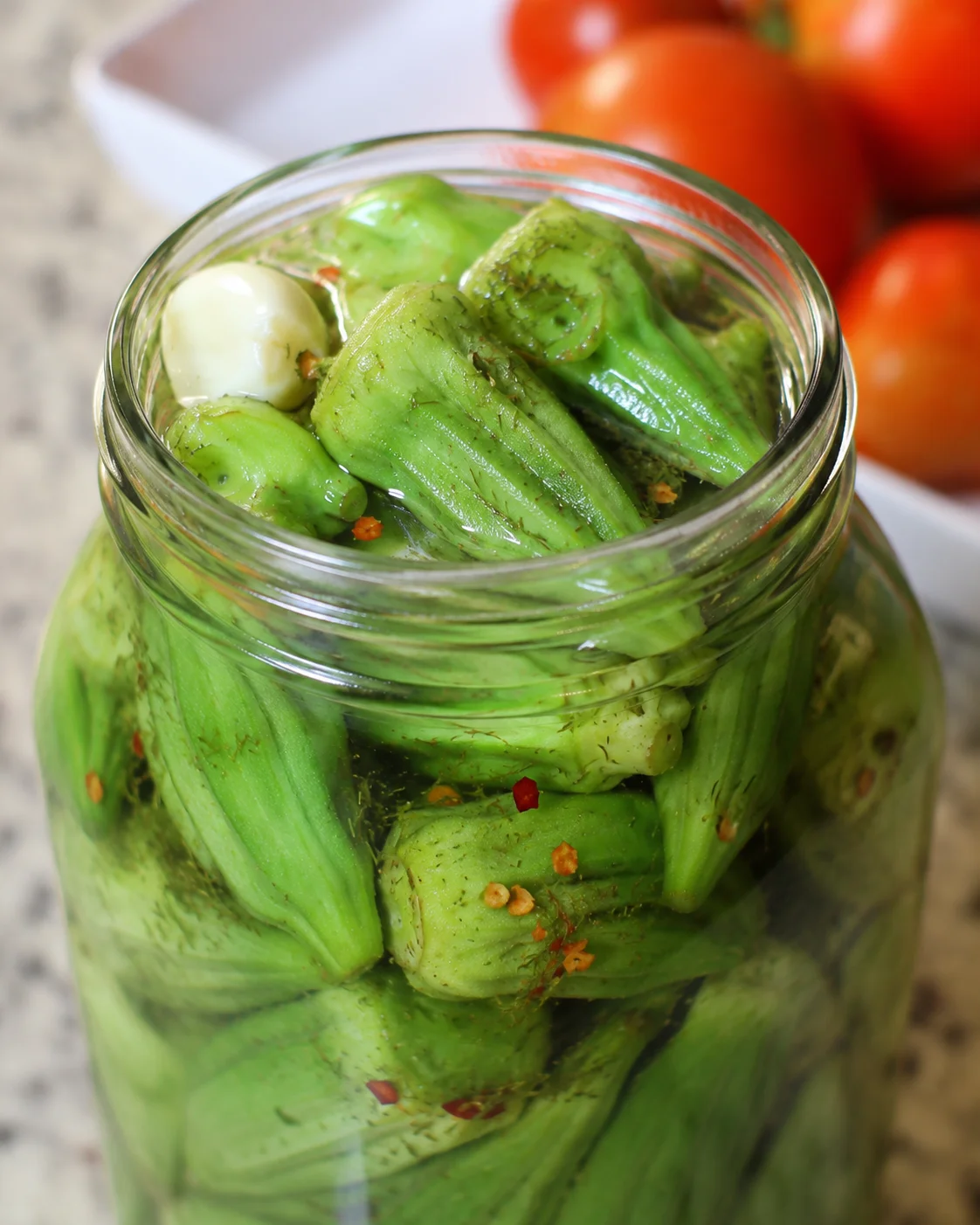 Close-up of vibrant green pickled okra sealed in a jar with seasoning.