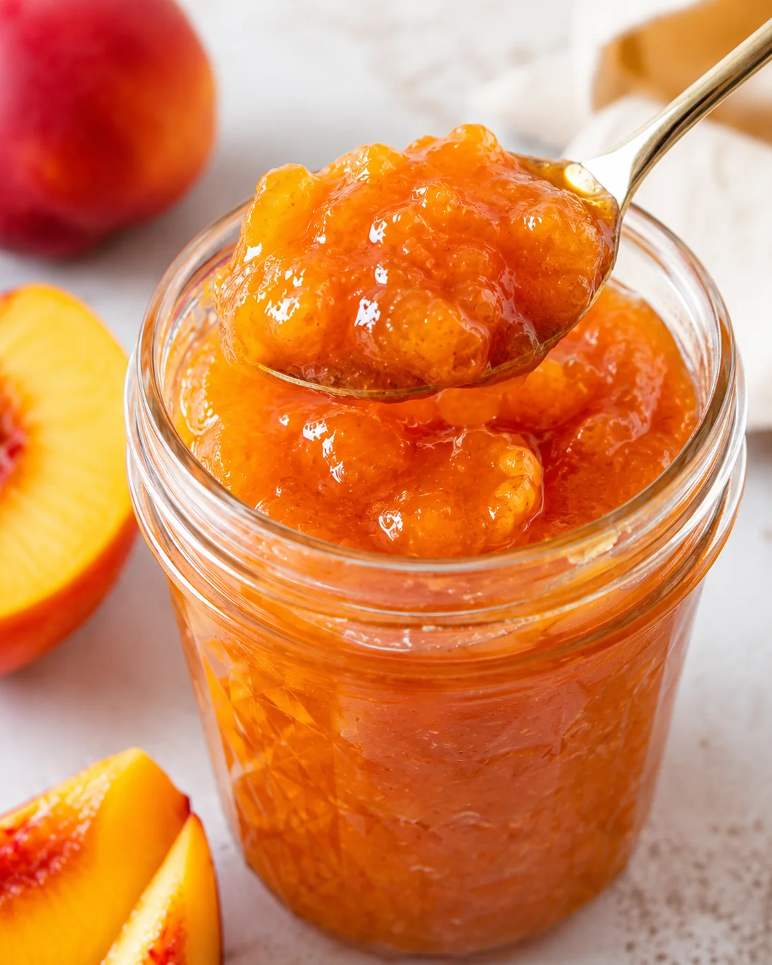 Bright, golden jar of homemade nectarines jam with a spoonful on top.