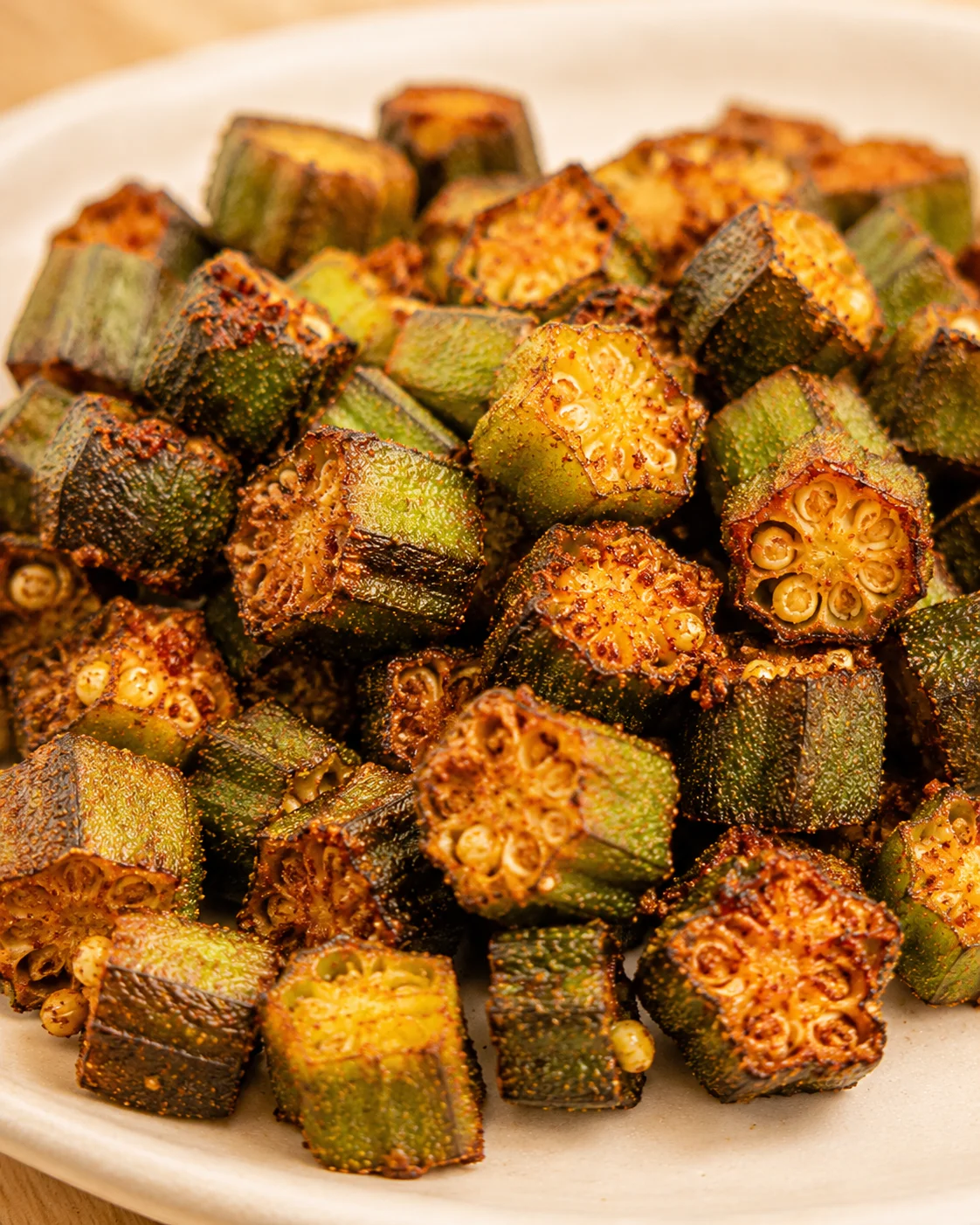 Crispy, smoky roasted okra pieces on a white plate, showcasing their golden edges.