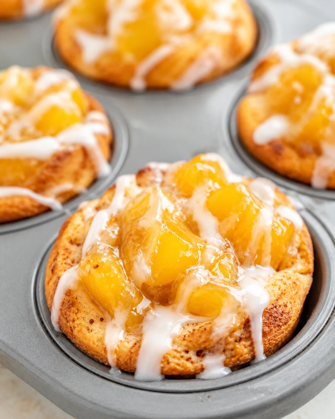 Delicious mini peach pies topped with peach chunks and icing, baked in muffin tins.