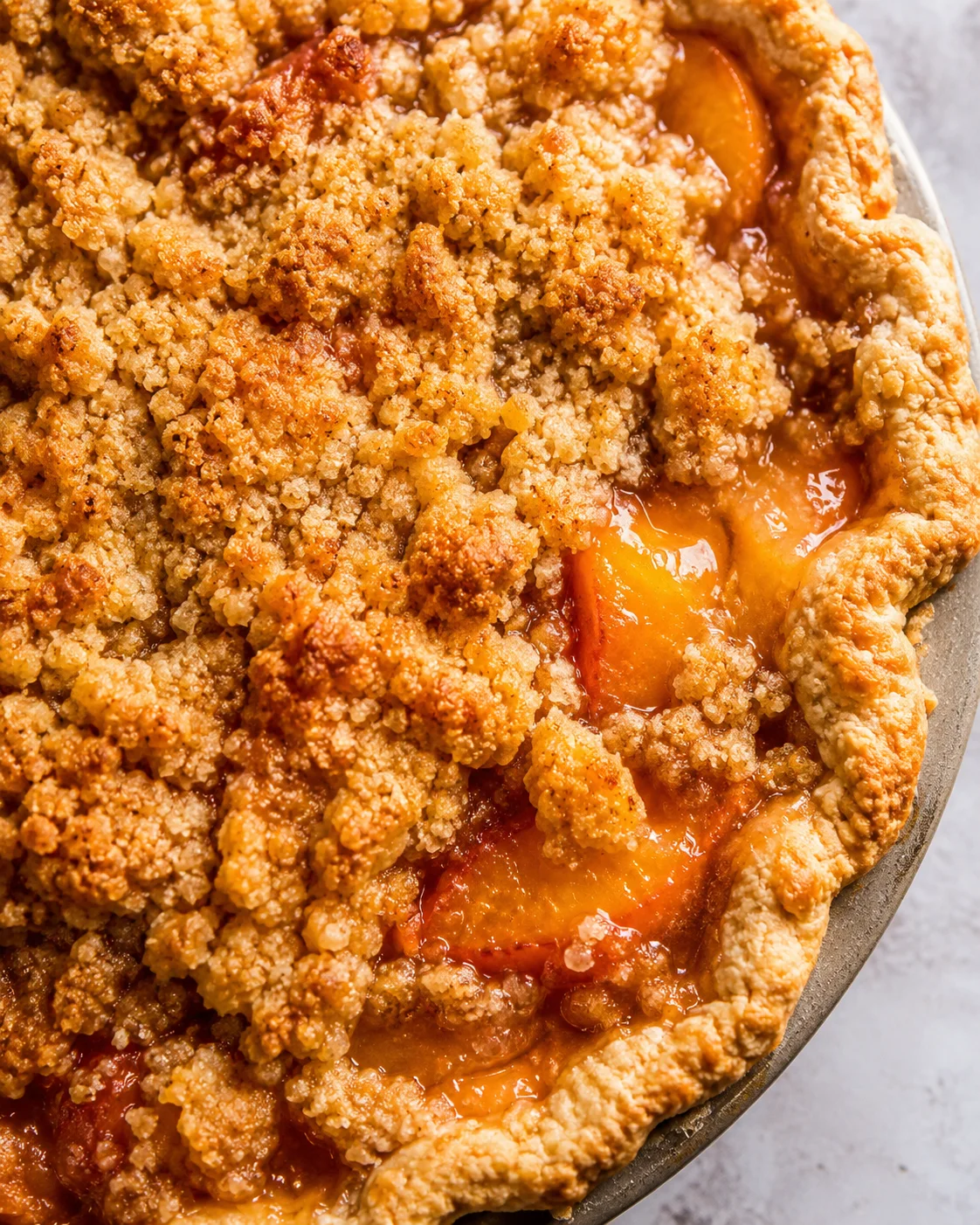 Close-up of homemade peach pie with buttery crumble topping, ready to serve.