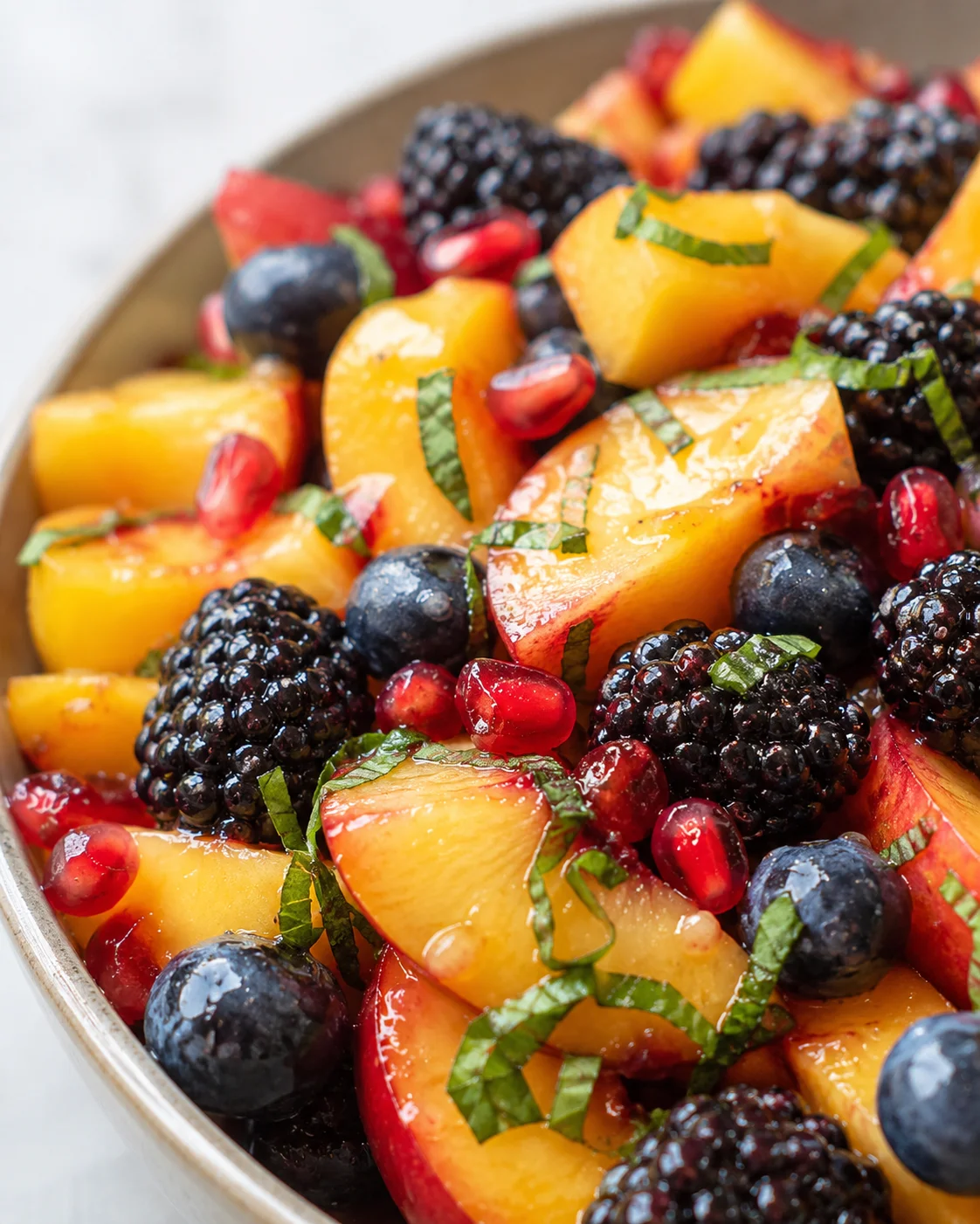 Honey Lime Basil Peach Fruit Salad Colorful mix of fresh peaches, blackberries, blueberries, pomegranate seeds, and basil in a bowl