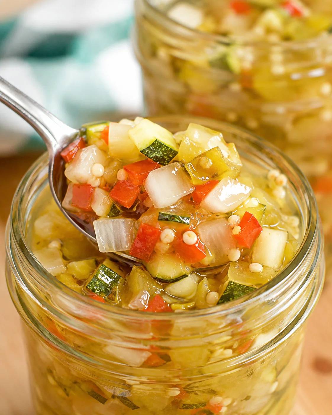 Close-up of colorful diced zucchini relish in a glass jar with a spoon