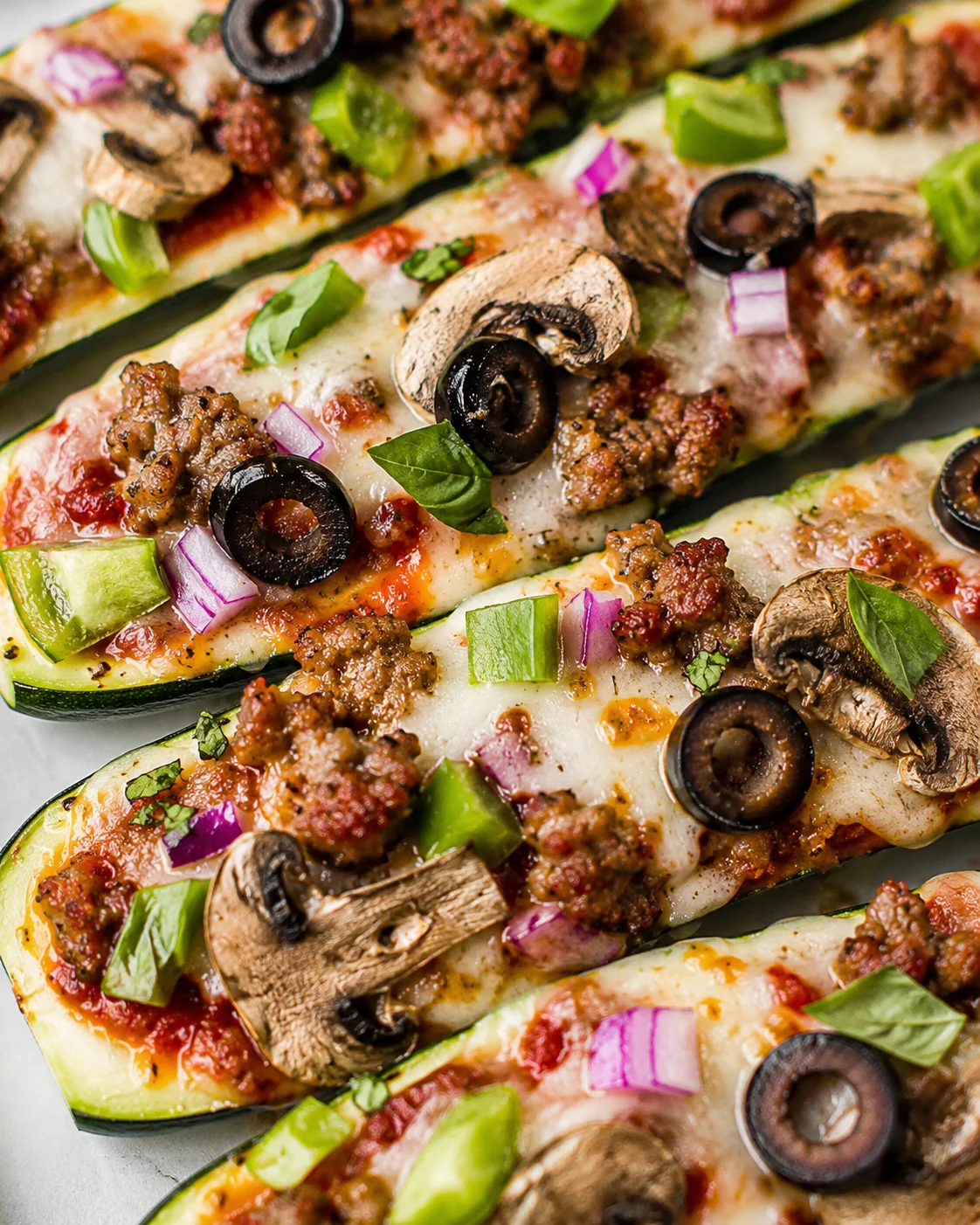 Close-up of zucchini pizza boats topped with sausage, mushrooms, olives, and peppers.