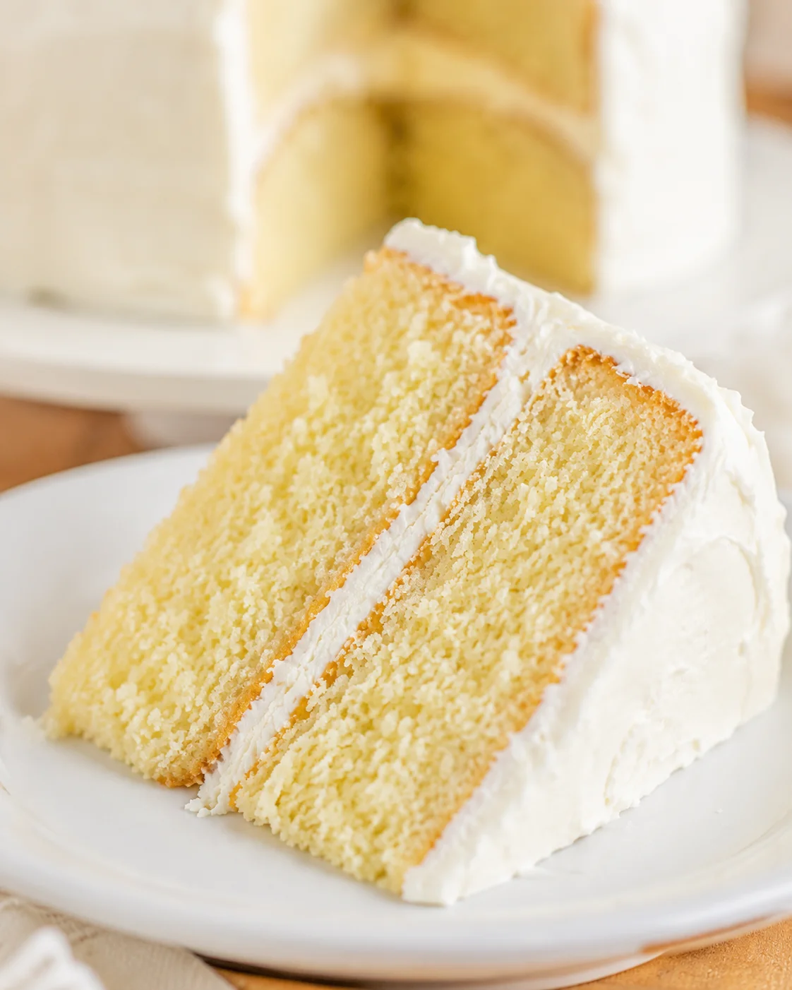 Slice of homemade vanilla cake with creamy frosting on a white plate