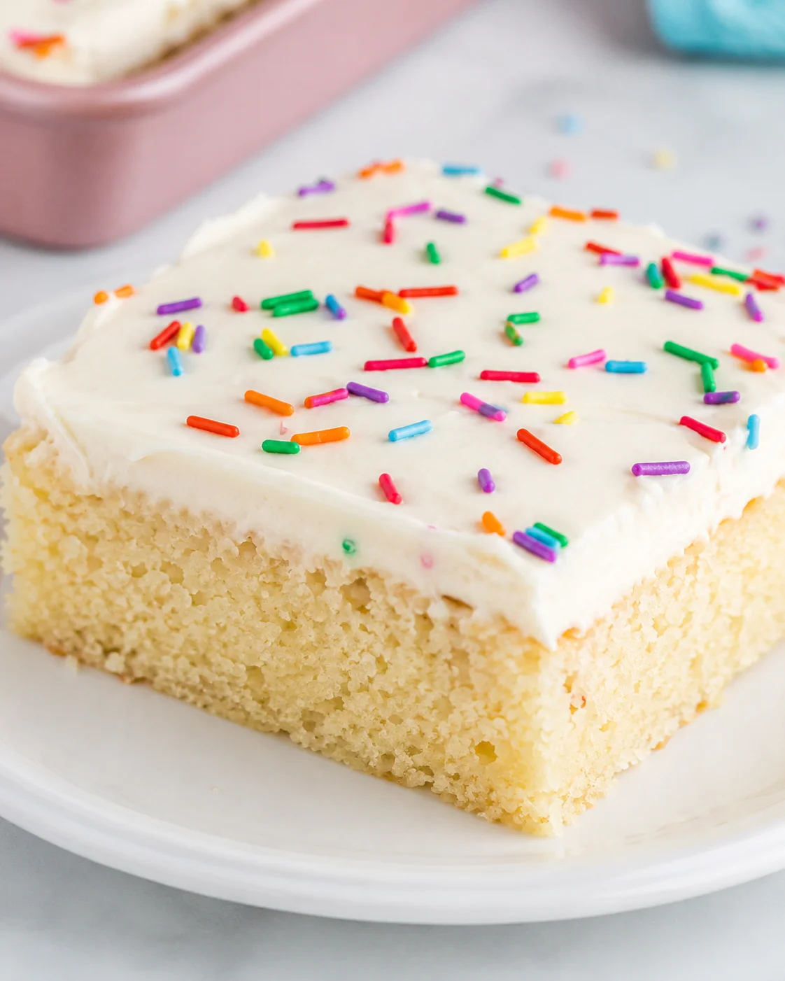 A fluffy vanilla sheet cake topped with colorful sprinkles on a white plate