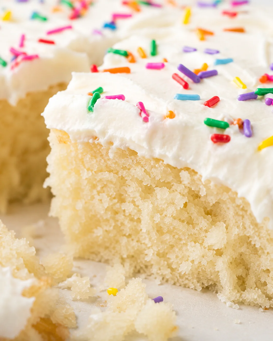 Close-up of a fluffy vanilla sheet cake with white frosting and colorful sprinkles