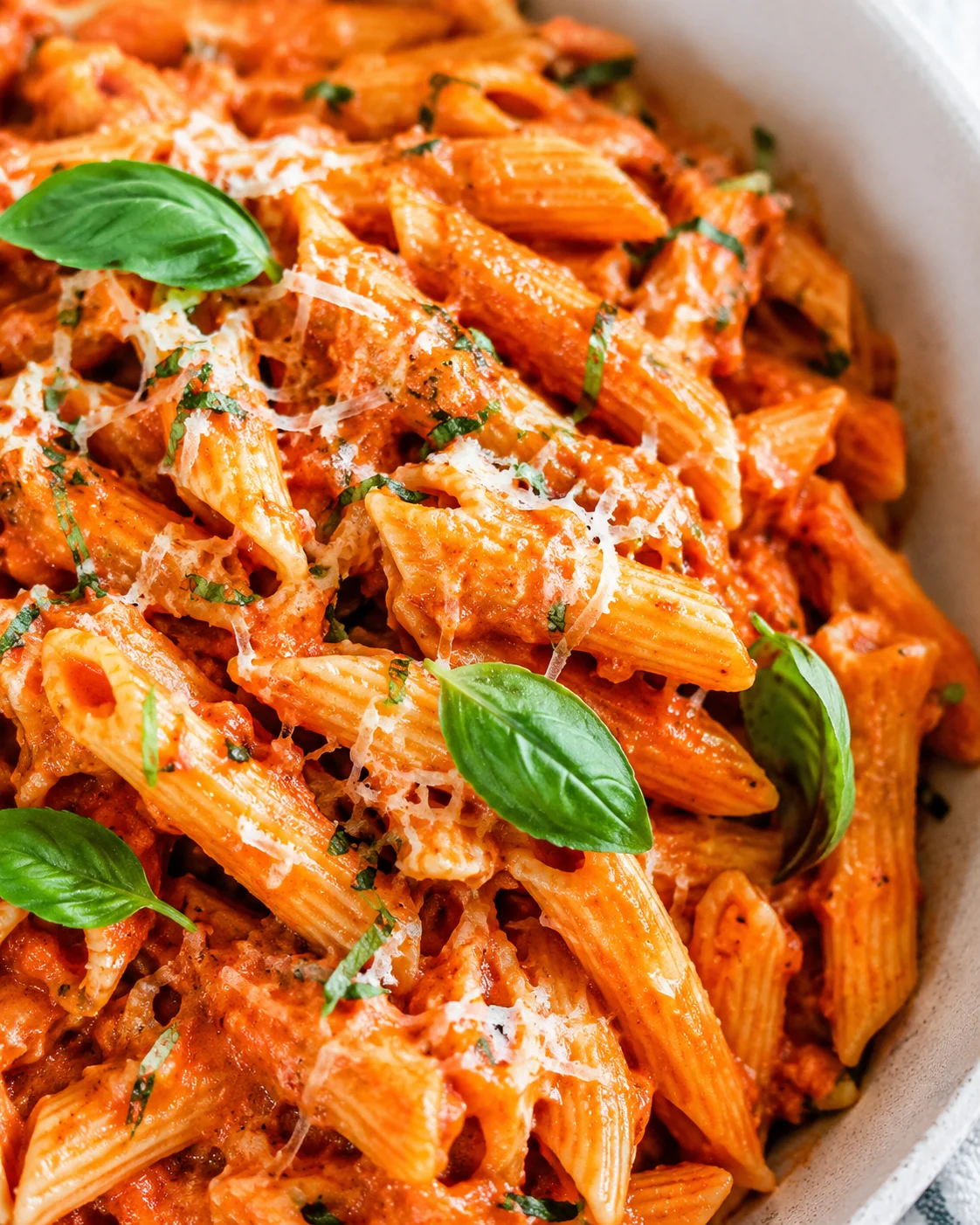 Close-up of flavorful penne pasta in red sauce garnished with basil and cheese
