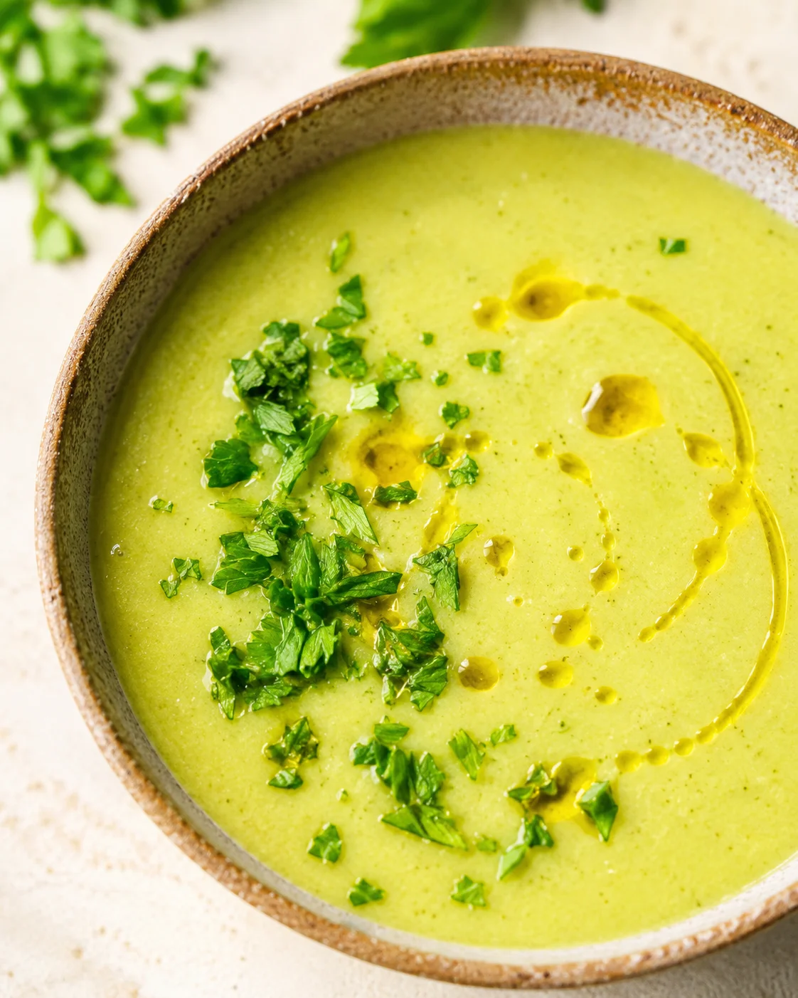 A bowl of vibrant green creamy zucchini soup garnished with fresh herbs and olive oil.