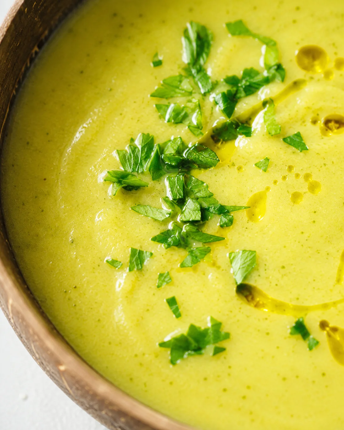 Fresh green zucchini soup garnished with chopped herbs in a rustic bowl.