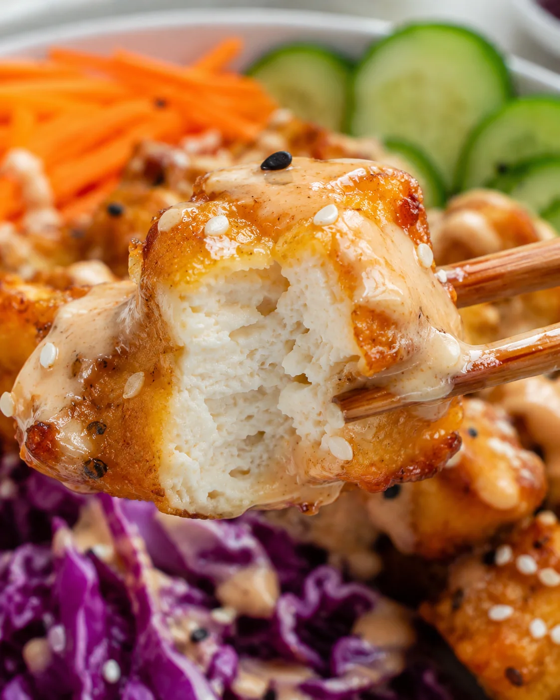 Crispy Bang Bang Tofu Recipe Close-up of crispy tofu coated in creamy sauce, with side vegetables in background.