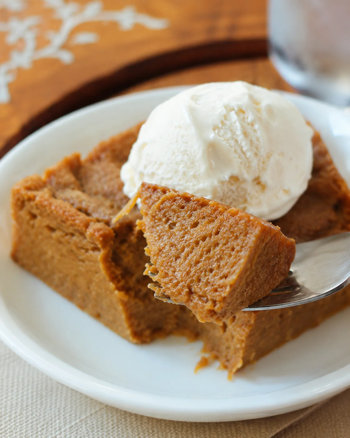 Fork lifting a bite from a plated slice of crustless pumpkin pie topped with vanilla ice cream