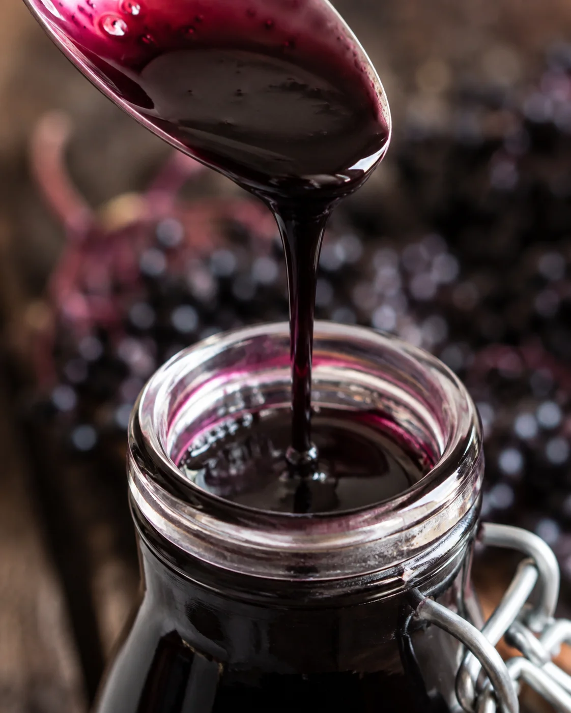 Thick elderberry syrup dripping from a spoon into a jar showing the syrup's smooth texture