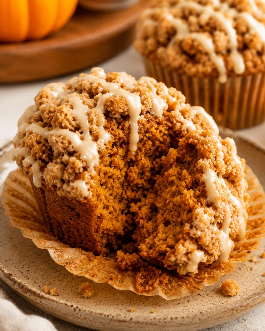 Gluten free pumpkin muffin with liner peeled back and a bite taken, showing moist interior and streusel with glaze