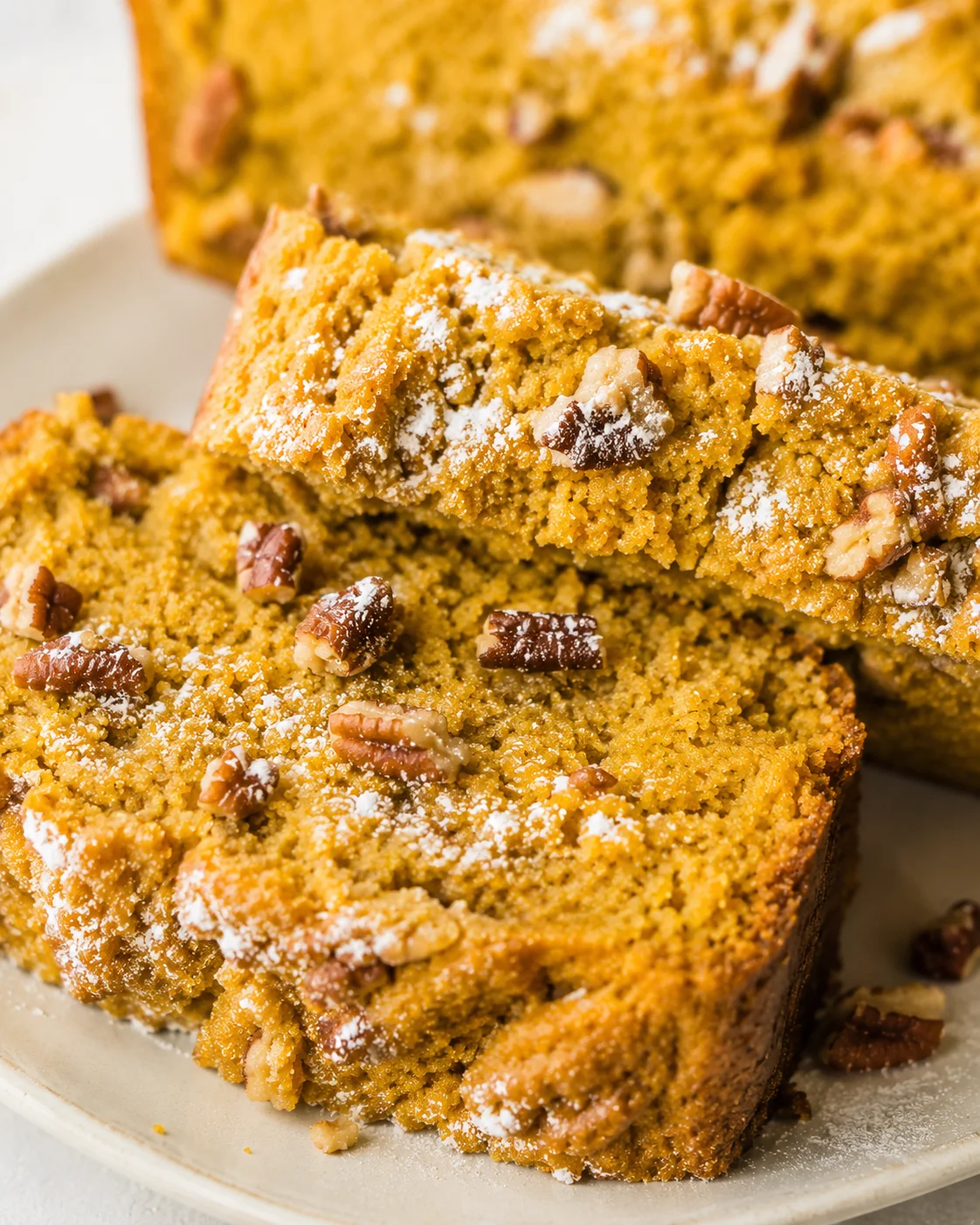 Two slices of keto pumpkin bread on a plate with the loaf in the background