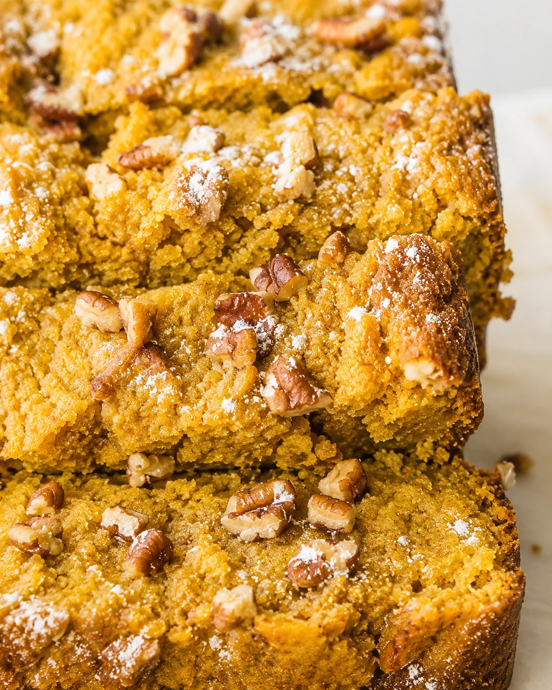 Close-up stacked slices of keto pumpkin bread topped with pecans and powdered sweetener